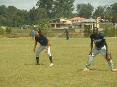 two people standing in the grass with baseball gloves on and one person holding a bat