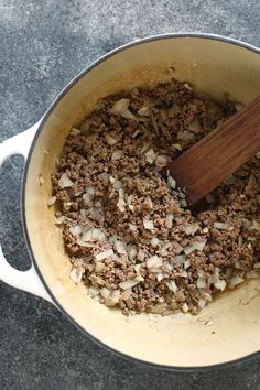 a pot filled with ground beef and onions next to a wooden spoon on a table