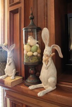 two bunny figurines sitting on top of a mantle next to a lantern filled with eggs