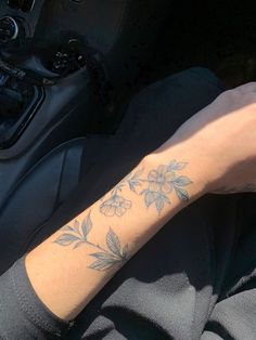 a person with a flower tattoo on their arm sitting in a car, next to a steering wheel