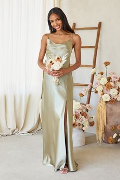 a woman standing in front of a flower arrangement wearing a long dress with side slit