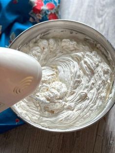 a mixing bowl filled with whipped cream on top of a wooden table