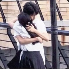 two people hugging each other in front of some stairs