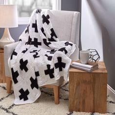 a white and black blanket sitting on top of a chair next to a table with a lamp