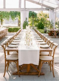 a long table is set with white linens and wooden chairs for an outdoor wedding reception