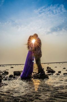 a man and woman kissing on the beach in front of the sun with their arms around each other