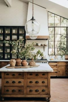 a kitchen with an island and lots of pots on it's counter top, surrounded by windows