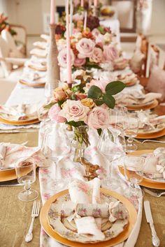 the table is set with pink flowers and white china plates, silverware, and candlesticks