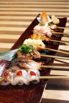 several different types of sushi are lined up on a long wooden tray with chopsticks