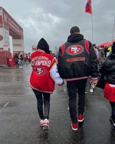 two people walking in the rain holding hands and wearing jackets with san francisco's logos on them