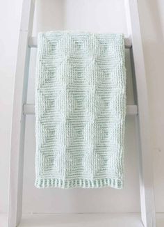 a white ladder with a green knitted blanket on it