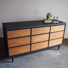 a black and wood dresser sitting on top of a cement floor next to a potted plant