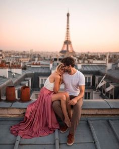 a man and woman sitting on top of a building with the eiffel tower in the background