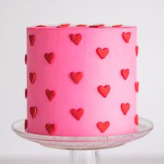 a pink cake with red hearts on it sitting on a glass stand, ready to be eaten