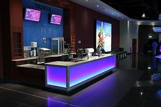 the inside of a restaurant with blue and purple lighting on the counter, televisions in the background