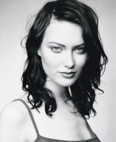 a black and white photo of a woman with long hair wearing a tank top looking at the camera