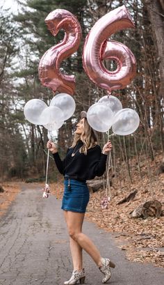 a woman is holding balloons in the air while standing on a road with her feet up