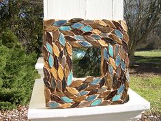 a decorative mirror sitting on top of a white bench in front of a green tree