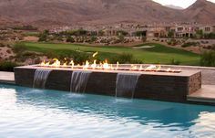 a fire pit in the middle of a pool with water running down it and mountains in the background