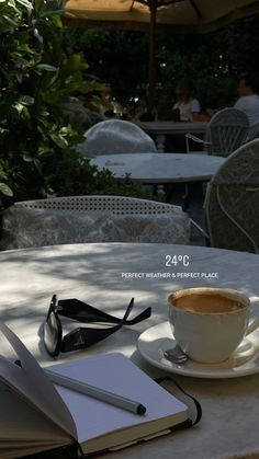 a cup of coffee sitting on top of a white table next to an open book