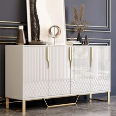 a white sideboard with gold handles and an art piece on top, against a blue wall