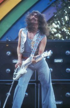 a man with long hair playing an electric guitar in front of a rainbow colored wall