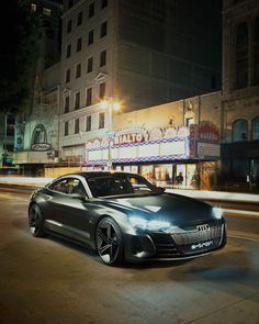 a silver car parked on the street in front of a movie theater at night with its lights on