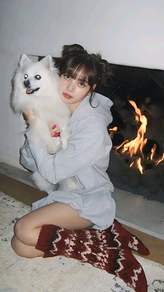 a woman sitting on the floor holding a white dog in front of a fire place