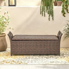 a brown wicker bench sitting on top of a rug next to potted plants