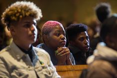 several people are sitting in a church and one is looking at the camera with pink hair