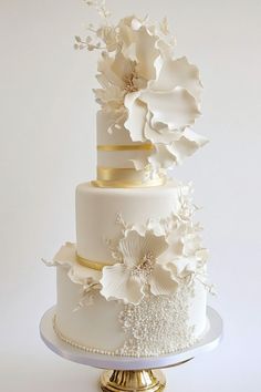 Three-tiered white wedding cake with gold accents and elaborate white floral decorations. Simple Traditional Wedding Cake, Wedding Cakes Simple Elegant Modern, Luxury Cake Design, Glamorous Wedding Cakes, Wedding Cake Designs Elegant, Chic Wedding Cake, Perfect Wedding Cake, Cotton Gin