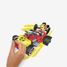 a hand is holding a toy car with mickey mouse on the front and yellow stripes behind it