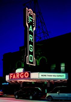 the marquee for fargo is lit up at night with cars parked in front