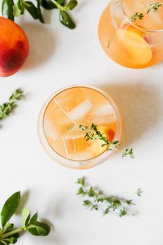 two glasses filled with drinks sitting on top of a white table next to peaches