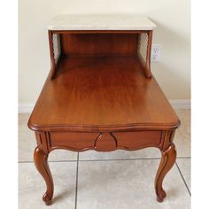 a wooden table with a shelf on the top and drawer at the bottom, in front of a white wall