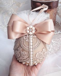 a hand holding an ornament that is decorated with pearls, lace and a bow