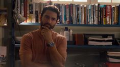 a man standing in front of a bookshelf with his hand on his chin