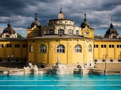 a large yellow building sitting next to a pool in front of a blue sky with clouds