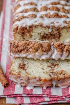 cinnamon roll bread with icing sitting on a red and white checkered towel next to cinnamon sticks