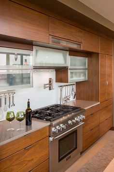 a modern kitchen with stainless steel appliances and wood cabinetry, along with wine glasses on the counter