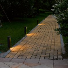 some lights that are on the side of a brick path in the grass and trees