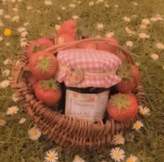 a basket filled with strawberries and jam on top of a grass covered field next to daisies