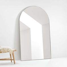 an arched mirror sitting on top of a white wall next to a wooden bench and chair