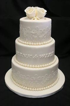 a three tiered wedding cake with white flowers on top and pearls around the edges