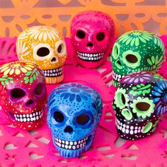 five brightly colored skulls are sitting on a pink doily and one is facing the camera