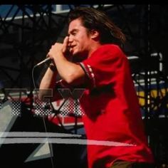 a man in red shirt holding a microphone up to his ear while standing on stage