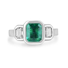 an emerald and diamond ring with three baguets on the side, set in white gold