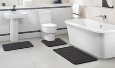 a white bath tub sitting next to a toilet under a bathroom window with blue rugs on the floor