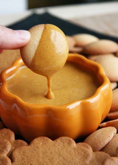 a person dipping some kind of sauce in a bowl with cookies on the table next to it