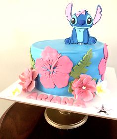 a blue cake with pink flowers and an elephant on top is sitting on a table